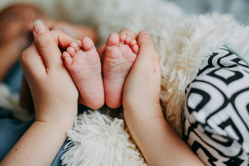 lengan seorang ibu yang sedang menggenggam kaki bayinya di kasur